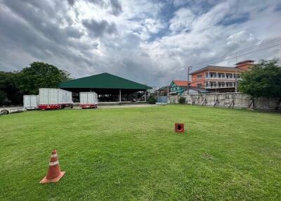 An outdoor view with a grassy area, building with green roof in the background, and some trucks