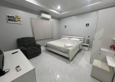 A modern bedroom with a bed, recliner, TV, and air conditioning