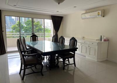 Spacious dining room with a large table and chairs, featuring a view of greenery and cityscape from the balcony