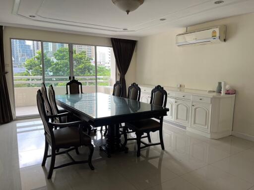 Spacious dining room with a large table and chairs, featuring a view of greenery and cityscape from the balcony