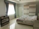 Spacious bedroom with large window, wardrobe, bed, and baby crib