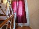 Staircase area with wooden railing and red curtains