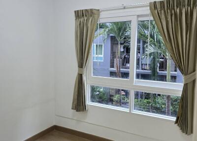 Small bedroom with wooden floor and window showing palm trees