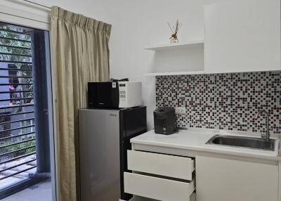 Modern kitchen with base cabinets, refrigerator, microwave, and mosaic backsplash