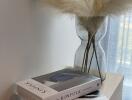 Close-up of a decorative side table with books and dried pampas grass