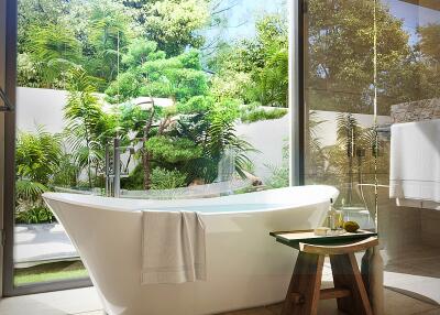 Modern bathroom with a freestanding bathtub next to a large window with a garden view