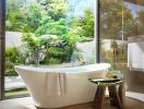 Modern bathroom with a freestanding bathtub next to a large window with a garden view