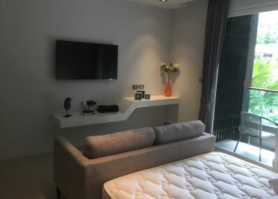 Modern bedroom with a wall-mounted TV, gray sofa, and large window.