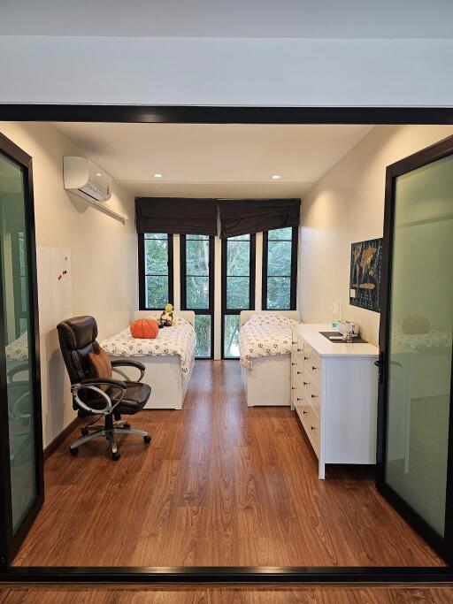 Bedroom with twin beds, modern office chair, dresser, and hardwood floors