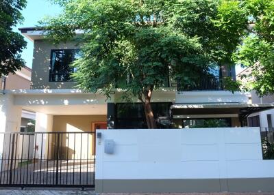 Exterior view of a modern two-story house with trees and a gated entrance