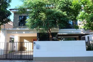 Exterior view of a modern two-story house with trees and a gated entrance