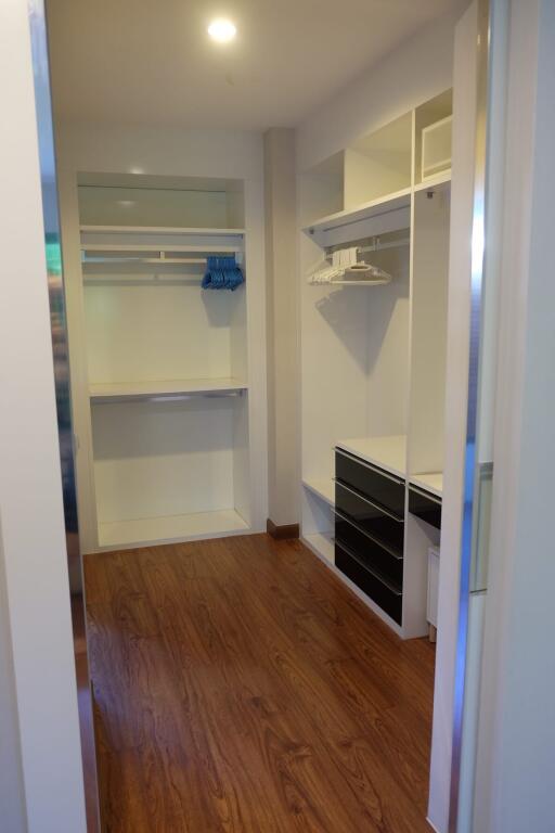 Walk-in closet with wooden flooring, built-in shelves, and drawers