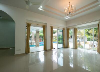 Spacious living room with chandelier and large windows overlooking the garden and pool