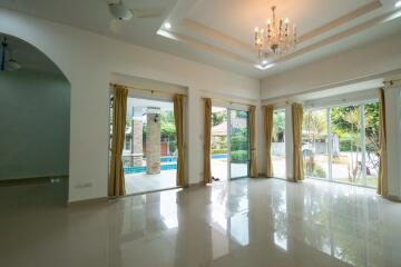 Spacious living room with chandelier and large windows overlooking the garden and pool