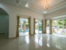 Spacious living room with chandelier and large windows overlooking the garden and pool