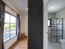 A bedroom with curtains and a window adjacent to a modern bathroom