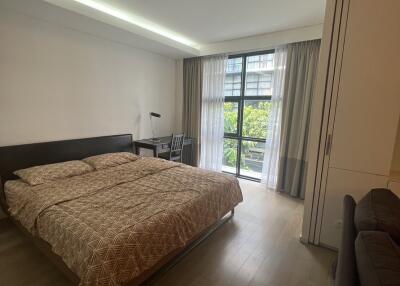 Modern bedroom with a large bed, desk, and a view through a window with curtains