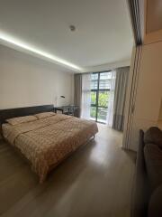 Modern bedroom with a large bed, desk, and a view through a window with curtains