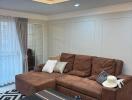 Modern living room with brown sectional sofa, black coffee table, stylish light fixture, and natural light from large windows.