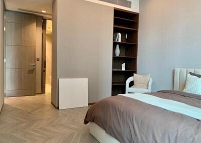 Modern bedroom with wooden flooring, a bed, open shelves, and a view into an adjacent bathroom.