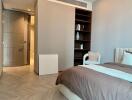 Modern bedroom with wooden flooring, a bed, open shelves, and a view into an adjacent bathroom.