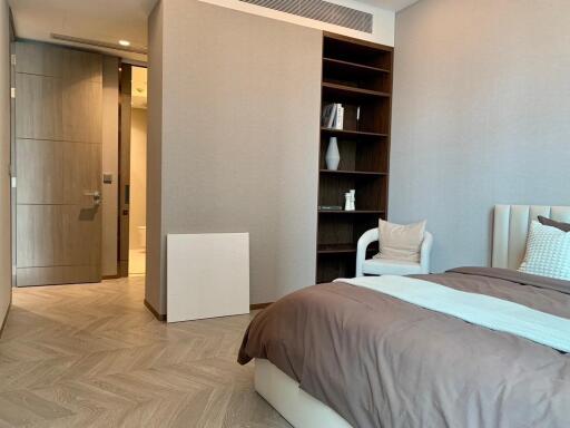 Modern bedroom with wooden flooring, a bed, open shelves, and a view into an adjacent bathroom.