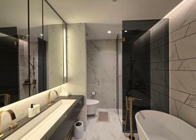 Modern bathroom with marble tiles, dual sinks, shower area, and free-standing bathtub