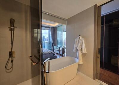 Modern bathroom with a standalone bathtub, glass-enclosed shower, and a view into a bedroom with floor-to-ceiling windows