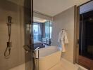 Modern bathroom with a standalone bathtub, glass-enclosed shower, and a view into a bedroom with floor-to-ceiling windows