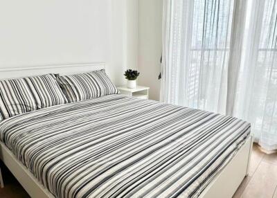 Bedroom with striped bedspread and bedside table next to a large window with sheer curtains