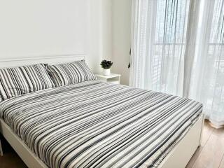 Bedroom with striped bedspread and bedside table next to a large window with sheer curtains