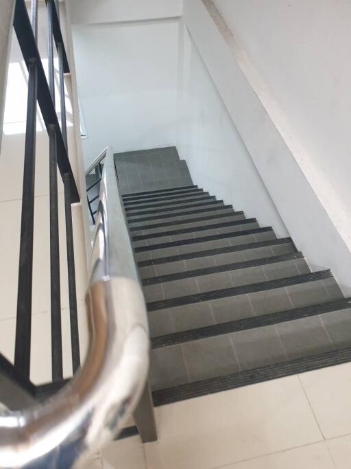 View of an indoor staircase with tiled steps and metal railings