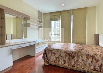 A cozy bedroom with a large bed, wooden flooring, and a well-lit dressing area.