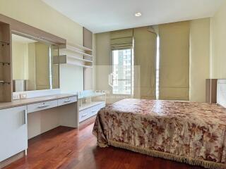 A cozy bedroom with a large bed, wooden flooring, and a well-lit dressing area.