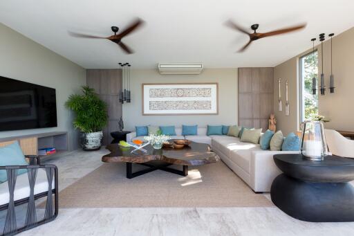 Modern living room with large wall-mounted TV, L-shaped sofa, air conditioning, and decorative elements