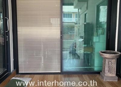 Image showing a sliding glass door entrance with a wooden floor, blinds, potted plant, and visible interior.