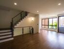 Spacious living room with a staircase, large windows, and wooden flooring