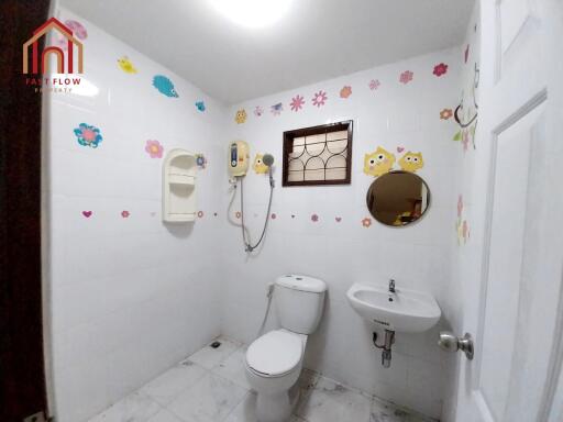 A well-lit bathroom with white tiles, toilet, sink, and wall decorations