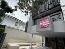 Modern facade of a building with 'For Sale' sign and clean landscaping