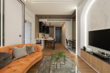 Modern living room with an open kitchen, brown sofa, wooden floors, and a mounted TV on the wall