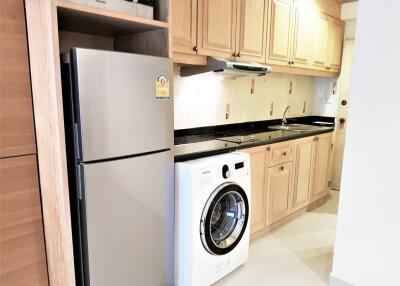 Modern kitchen with wooden cabinets, stainless steel refrigerator, and washing machine