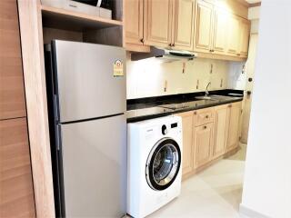 Modern kitchen with wooden cabinets, stainless steel refrigerator, and washing machine