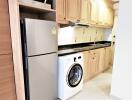 Modern kitchen with wooden cabinets, stainless steel refrigerator, and washing machine