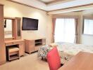 Well-lit bedroom with a TV, desk, and double bed