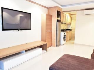 Modern living area with wall-mounted TV, kitchen, washing machine, and air conditioning