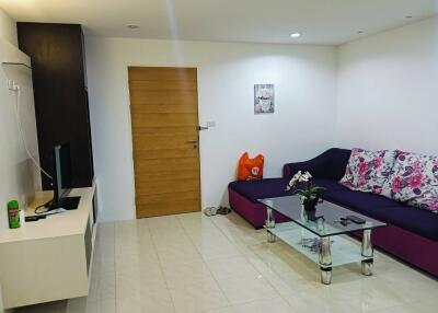 Modern living room with couch, glass coffee table, TV, and wooden door