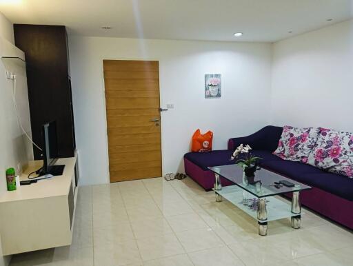 Modern living room with couch, glass coffee table, TV, and wooden door