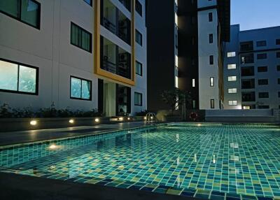 Modern apartment buildings overlooking a lit outdoor swimming pool at dusk