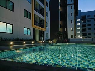 Modern apartment buildings overlooking a lit outdoor swimming pool at dusk