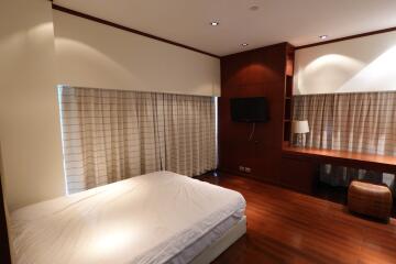 Spacious and modern bedroom with wooden flooring, large windows, and a mounted TV.